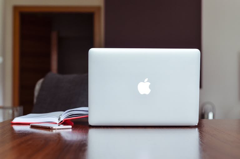 A clean and modern workspace featuring a laptop, book, and smartphone on a wooden table.