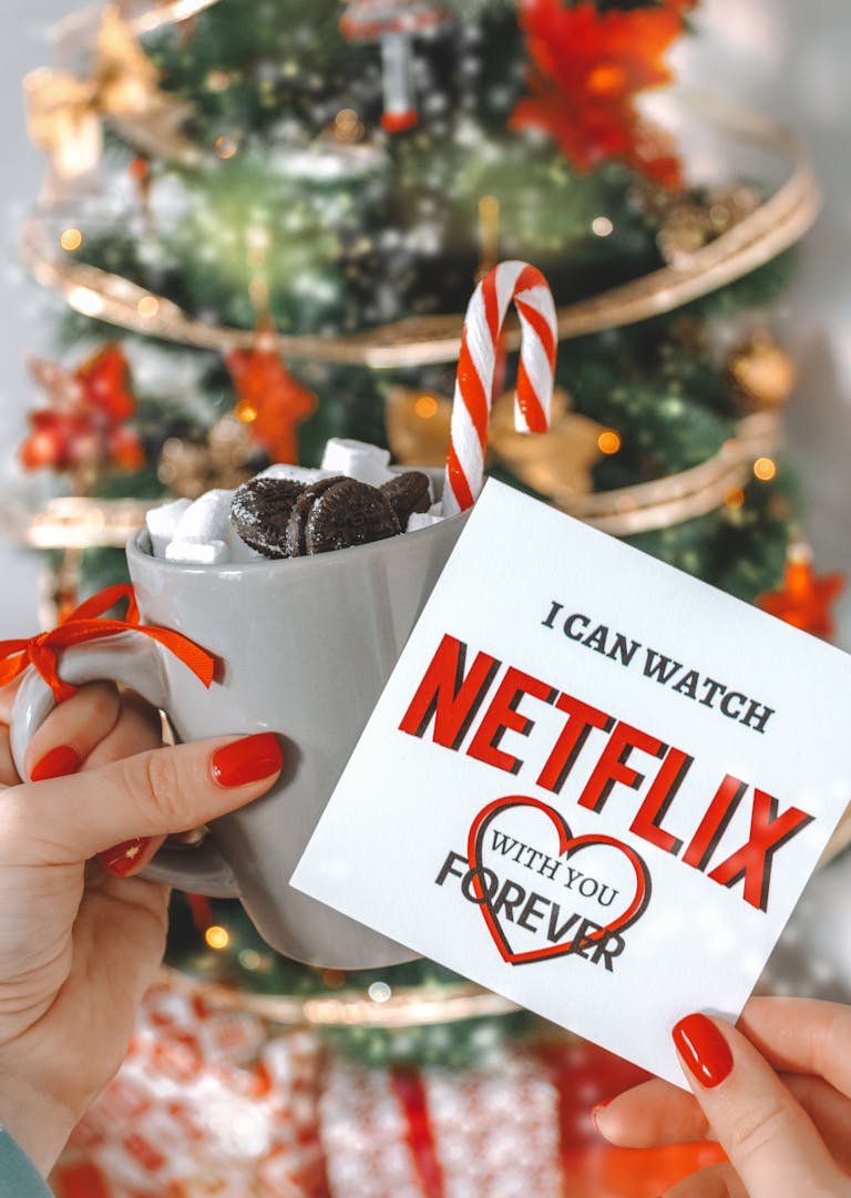 Festive Christmas card and hot chocolate with marshmallows in front of a decorated tree.